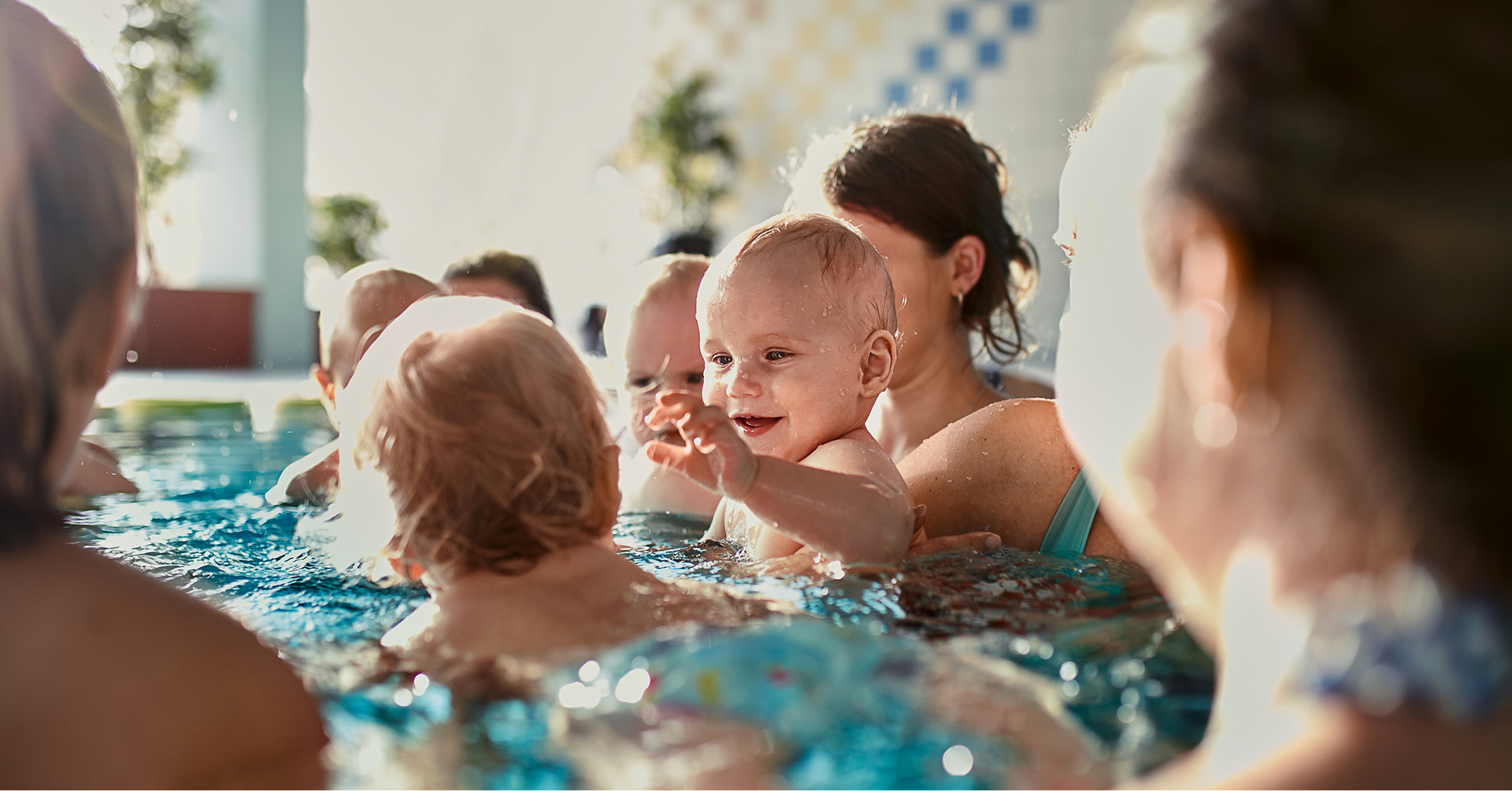 Mehrere Kleinkinder im Wasser, ein lächelndes Kleinkind ist im Bildfokus