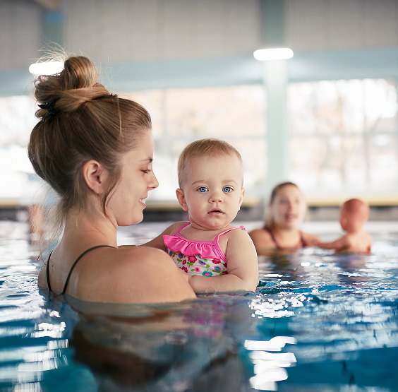 Eine steht bis zu den Schultern im Wasser, sie trägt ein Baby auf dem Arm