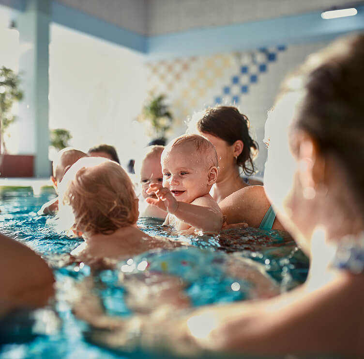 Mehrere Kleinkinder im Wasser, ein lächelndes Kleinkind ist im Bildfokus