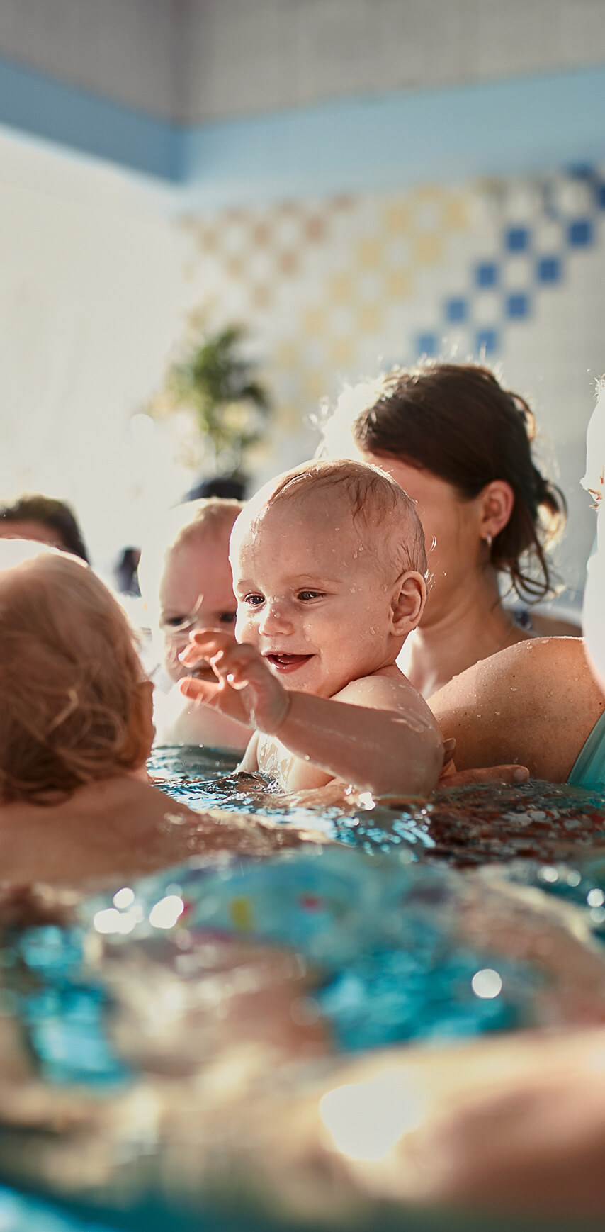 Mehrere Kleinkinder im Wasser, ein lächelndes Kleinkind ist im Bildfokus