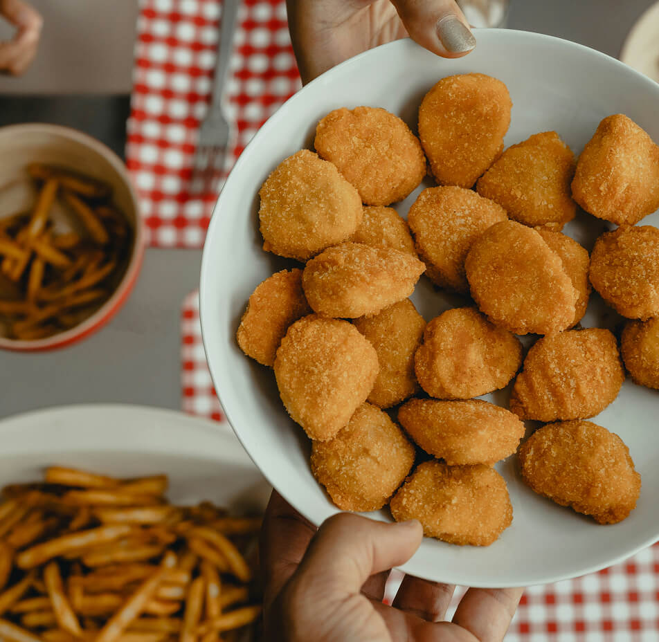 Eine Schüssel panierter Nuggets, daneben zwei Teller mit Pommes