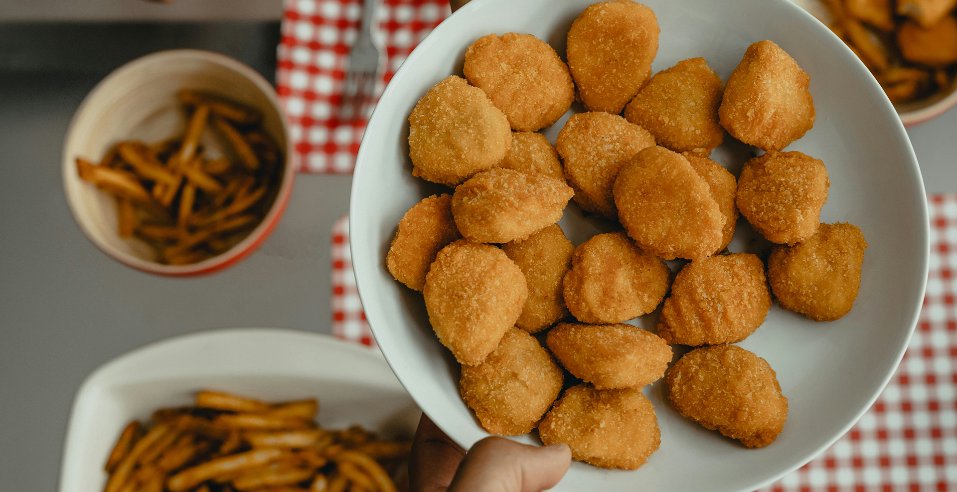 Eine Schüssel panierter Nuggets, daneben zwei Teller mit Pommes