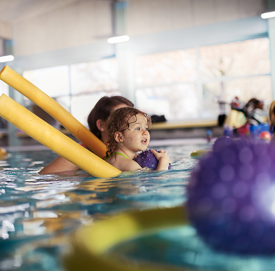 Ein Kind schwimmt mit Hilfe einer gelben Schwimmnudel